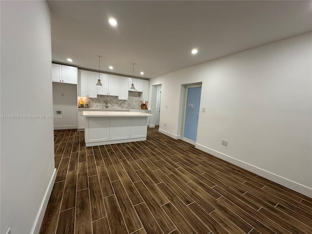 kitchen featuring backsplash, a center island with sink, white cabinets, dark hardwood / wood-style floors, and hanging light fixtures