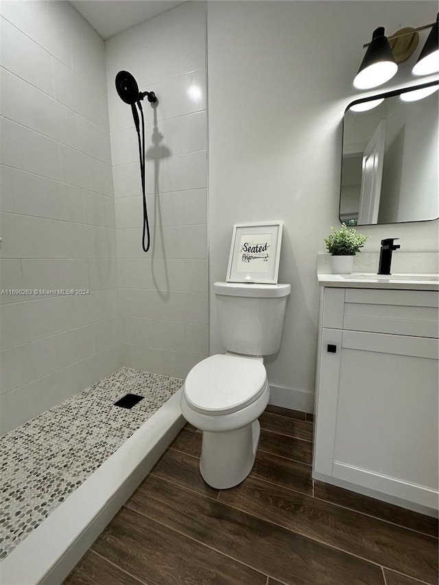 bathroom featuring hardwood / wood-style floors, vanity, toilet, and tiled shower