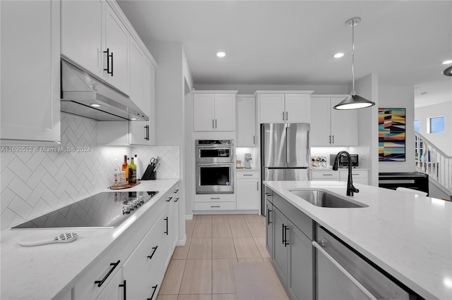 kitchen with white cabinets, sink, light stone countertops, appliances with stainless steel finishes, and decorative light fixtures