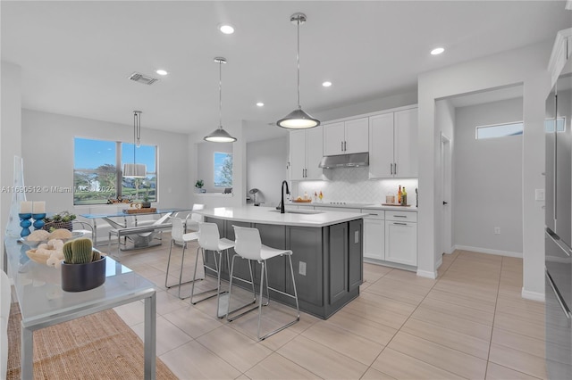 kitchen featuring sink, light tile patterned floors, decorative light fixtures, white cabinets, and an island with sink