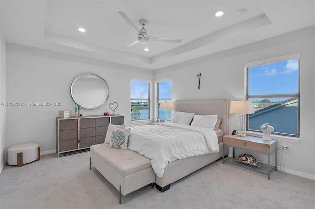 carpeted bedroom featuring a tray ceiling, ceiling fan, and a water view