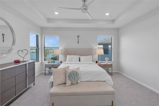 carpeted bedroom with ceiling fan, a water view, and a tray ceiling