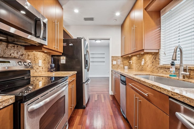 kitchen with light stone countertops, sink, dark wood-type flooring, decorative backsplash, and appliances with stainless steel finishes