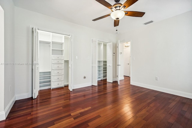 unfurnished bedroom with multiple closets, ceiling fan, and dark wood-type flooring