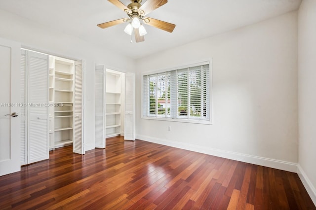 unfurnished bedroom with ceiling fan, dark hardwood / wood-style flooring, and two closets