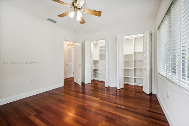 unfurnished bedroom featuring ceiling fan, dark hardwood / wood-style floors, and multiple closets