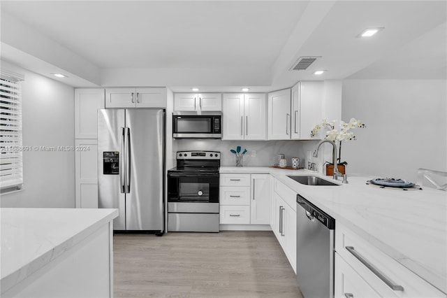 kitchen featuring light stone counters, stainless steel appliances, sink, white cabinets, and light hardwood / wood-style flooring