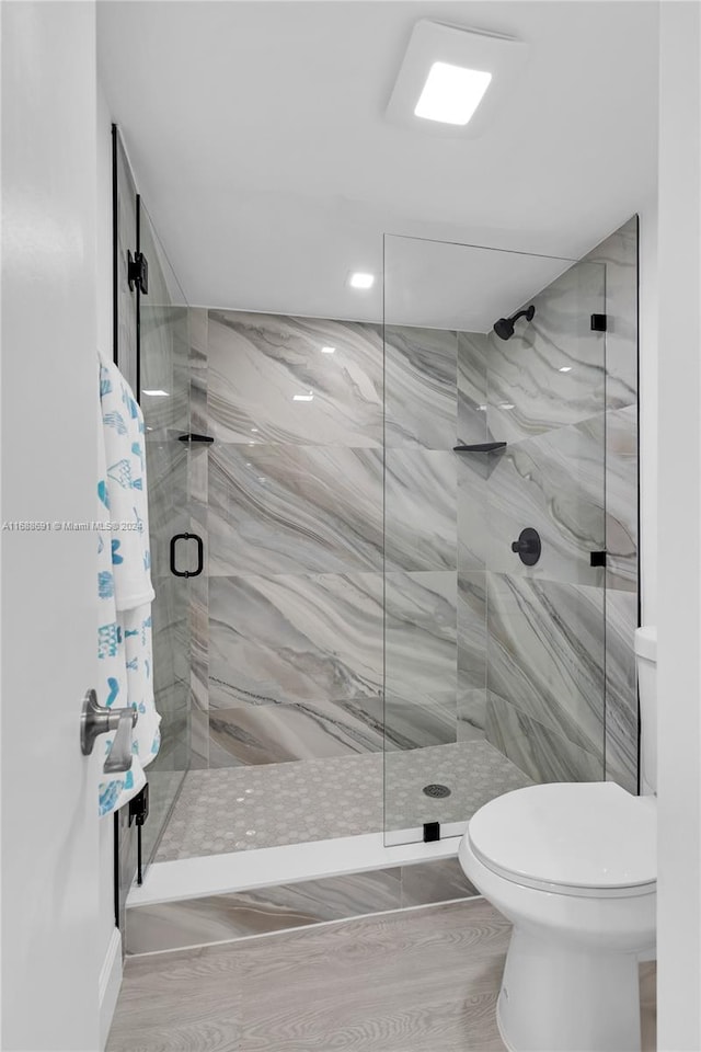 bathroom with toilet, hardwood / wood-style floors, and a tile shower