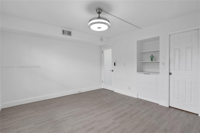 unfurnished room with built in shelves and wood-type flooring