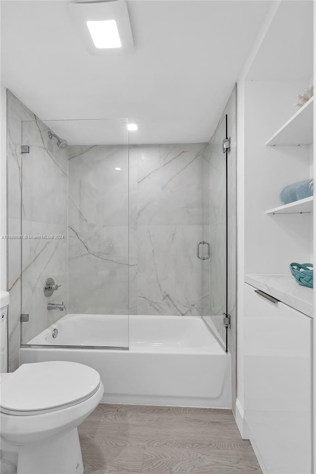 bathroom with bath / shower combo with glass door, hardwood / wood-style flooring, and toilet