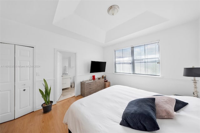 bedroom with light hardwood / wood-style floors, a tray ceiling, and connected bathroom