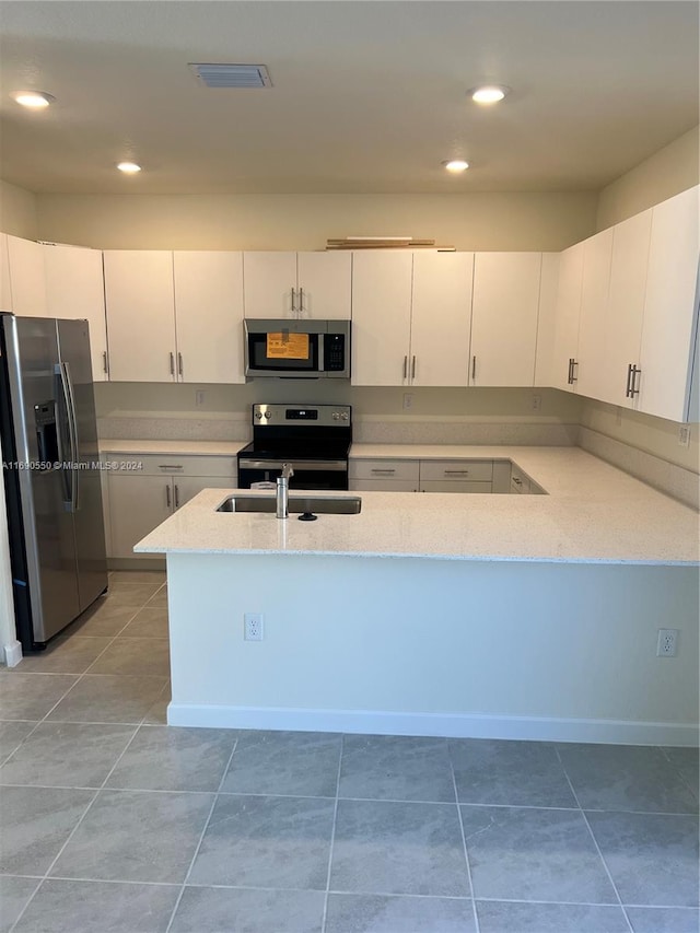 kitchen with stainless steel appliances, light stone counters, kitchen peninsula, light tile patterned floors, and white cabinetry