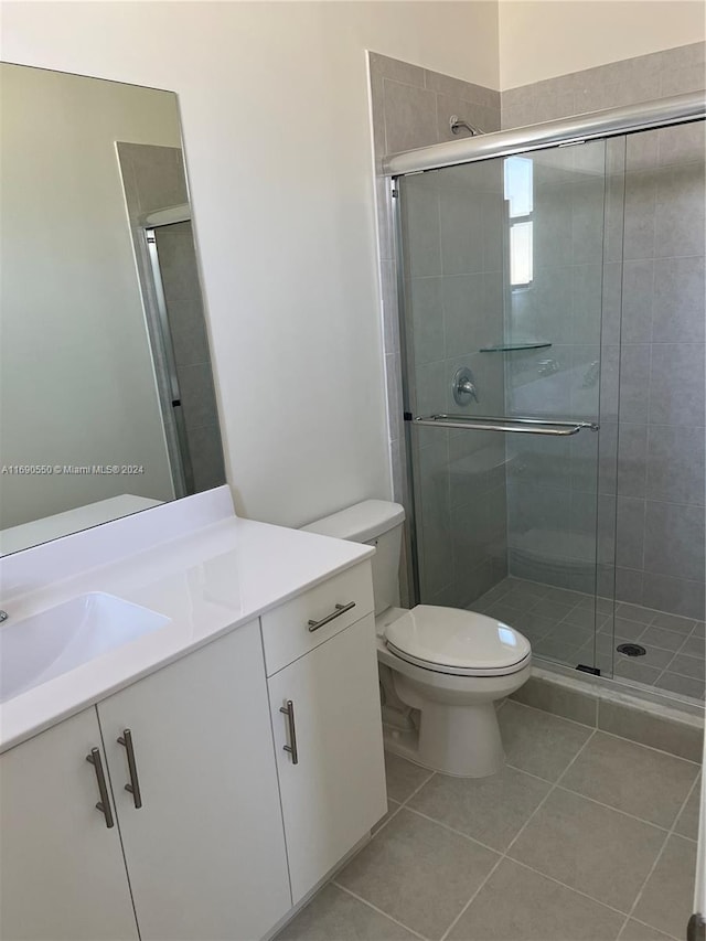 bathroom featuring a shower with door, vanity, tile patterned floors, and toilet