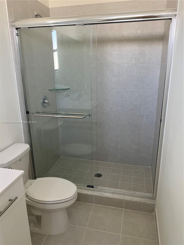 bathroom featuring a shower with shower door, vanity, tile patterned floors, and toilet