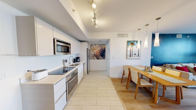 kitchen with white cabinetry, appliances with stainless steel finishes, hanging light fixtures, sink, and light hardwood / wood-style floors