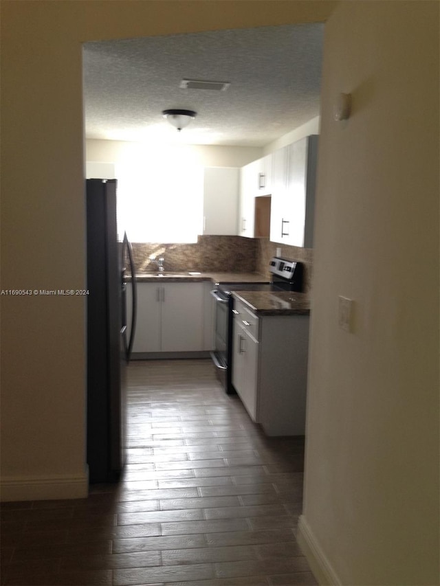 kitchen with dark hardwood / wood-style flooring, black fridge, white cabinets, backsplash, and stainless steel electric stove