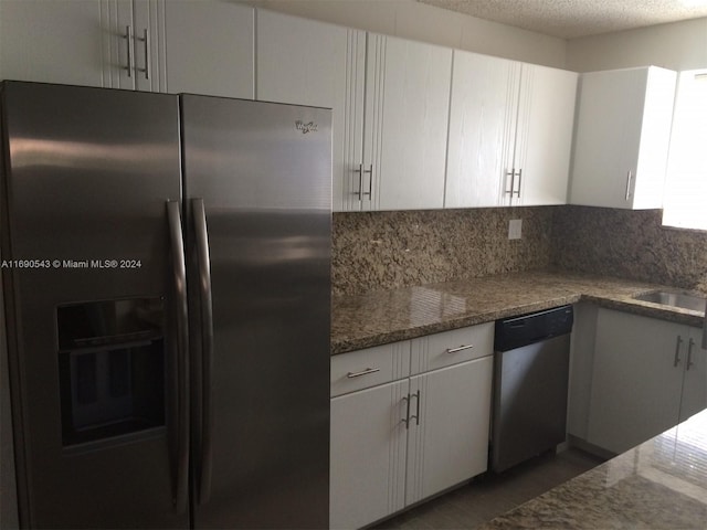 kitchen with stainless steel appliances, dark stone counters, backsplash, a textured ceiling, and white cabinets