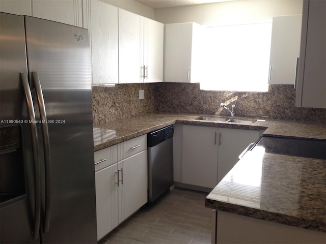 kitchen with stainless steel appliances, sink, tasteful backsplash, dark stone countertops, and white cabinets