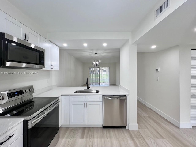 kitchen featuring white cabinetry, stainless steel appliances, sink, a chandelier, and light hardwood / wood-style flooring