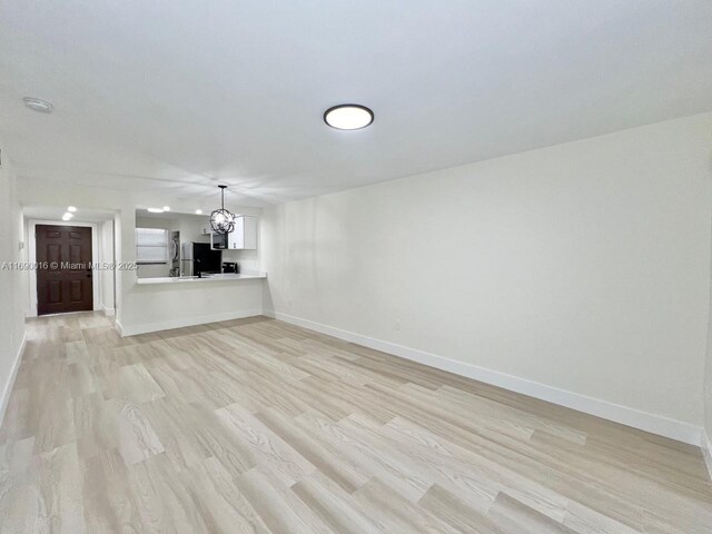 unfurnished living room featuring sink, light wood-type flooring, and a chandelier