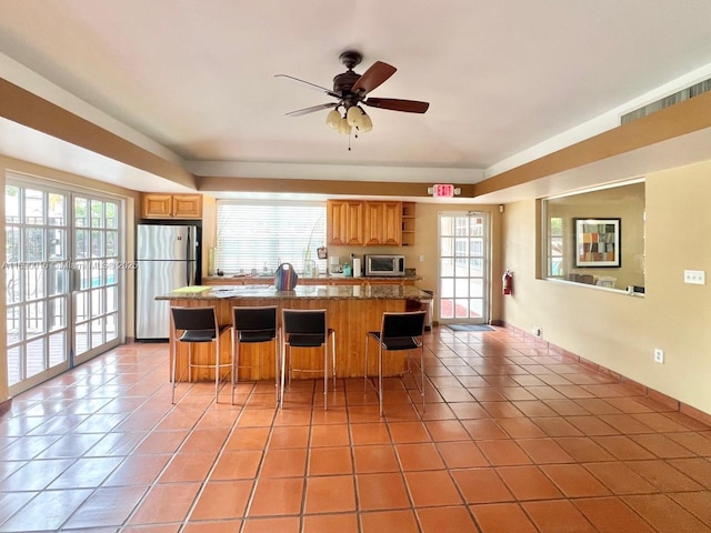 kitchen featuring ceiling fan, light tile patterned floors, a kitchen bar, a center island, and stainless steel appliances