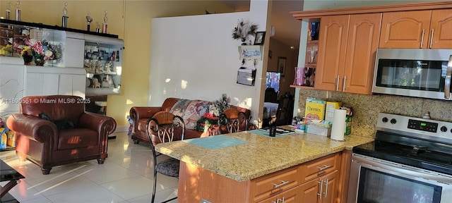 kitchen with light tile patterned floors, a kitchen breakfast bar, stainless steel appliances, light stone countertops, and decorative backsplash