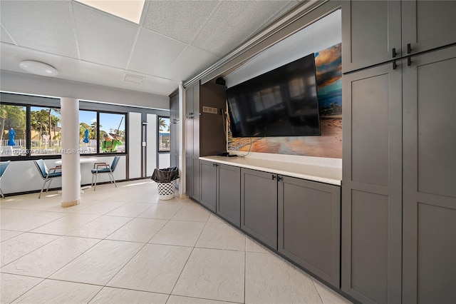 interior space with gray cabinetry, light tile patterned floors, and a paneled ceiling