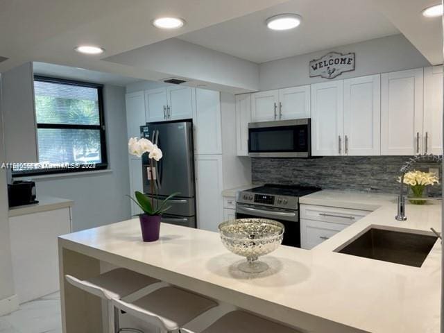 kitchen featuring a kitchen bar, stainless steel appliances, white cabinets, sink, and tasteful backsplash