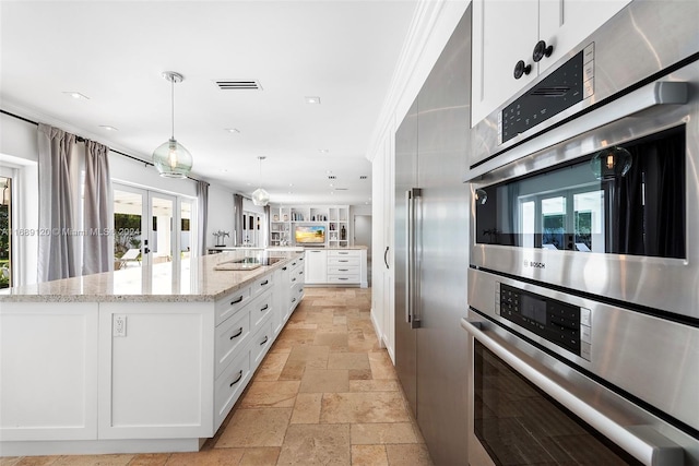 kitchen featuring a kitchen island with sink, light stone countertops, a healthy amount of sunlight, and white cabinets