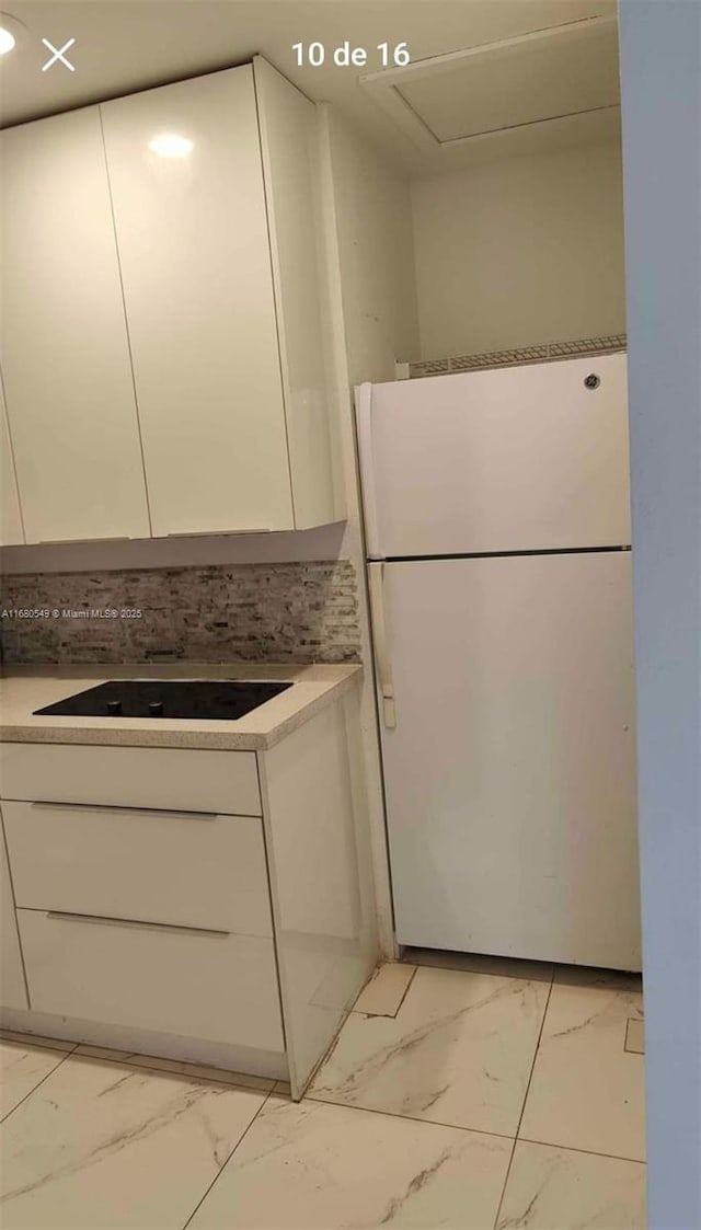 kitchen featuring black electric cooktop, decorative backsplash, white fridge, and white cabinets