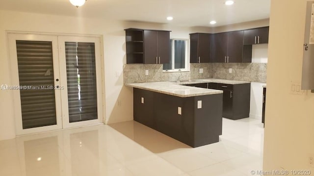 kitchen with tasteful backsplash, dark brown cabinetry, kitchen peninsula, light stone countertops, and french doors