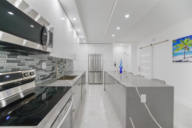 kitchen featuring stainless steel appliances, white cabinetry, sink, a barn door, and decorative backsplash