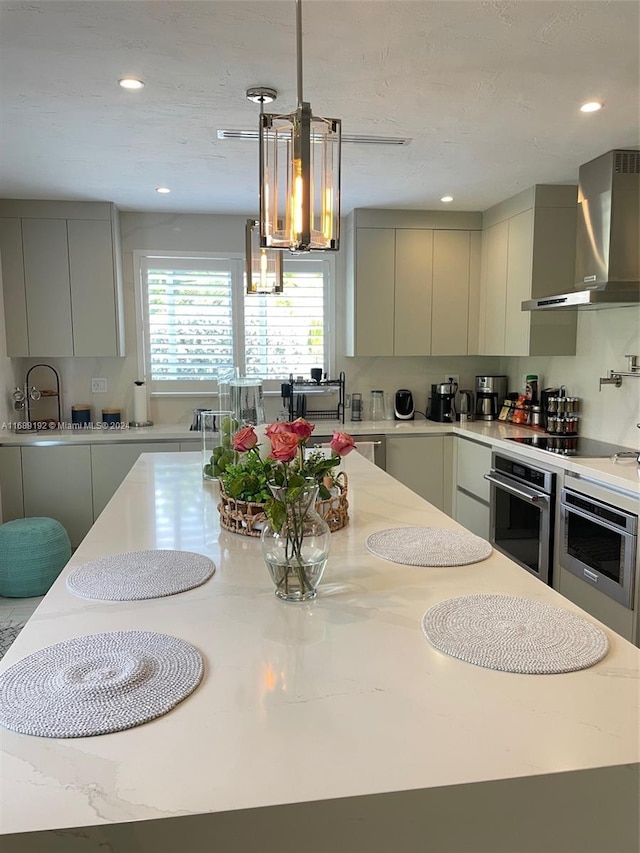 kitchen with stainless steel oven, wall chimney range hood, gray cabinetry, and a chandelier