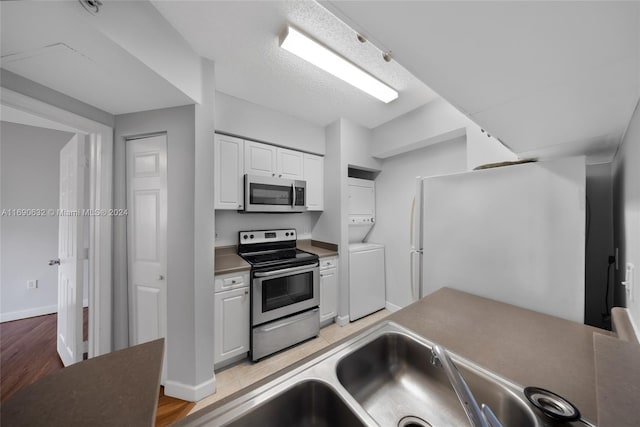 kitchen featuring stainless steel appliances, light hardwood / wood-style floors, stacked washer and clothes dryer, and white cabinetry