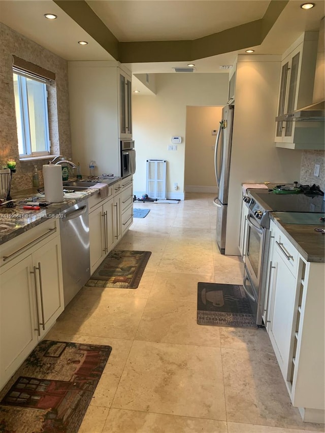 kitchen featuring dark stone counters, wall chimney range hood, appliances with stainless steel finishes, sink, and white cabinets