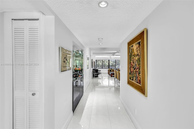 hall with a textured ceiling and light tile patterned floors