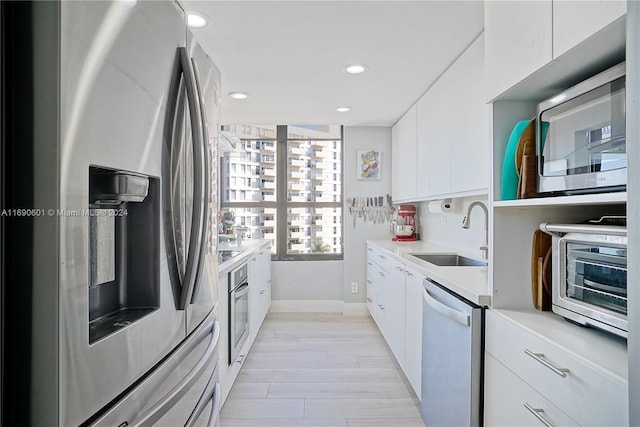 kitchen featuring white cabinets, stainless steel appliances, sink, and light hardwood / wood-style flooring