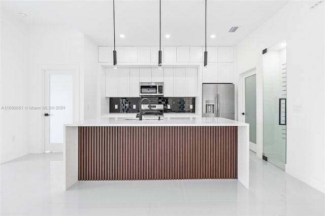 kitchen featuring stainless steel appliances, hanging light fixtures, white cabinets, and an island with sink