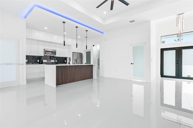 kitchen with a center island with sink, white cabinetry, appliances with stainless steel finishes, pendant lighting, and french doors