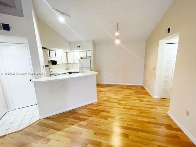 kitchen featuring white appliances, rail lighting, vaulted ceiling, light wood-type flooring, and white cabinetry