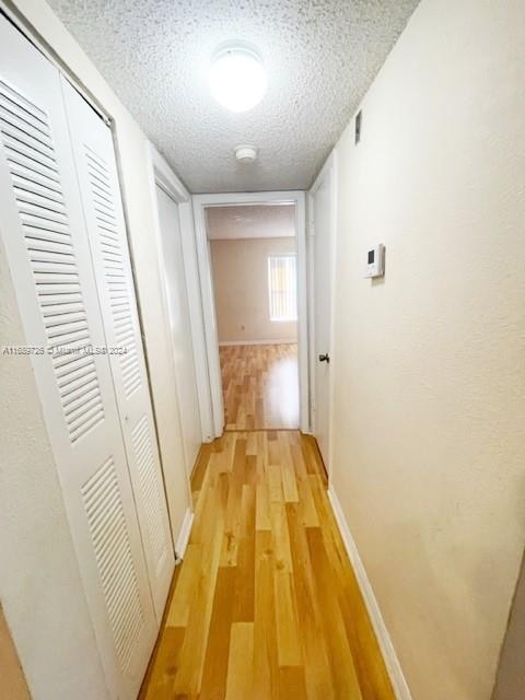 corridor with a textured ceiling and light hardwood / wood-style floors