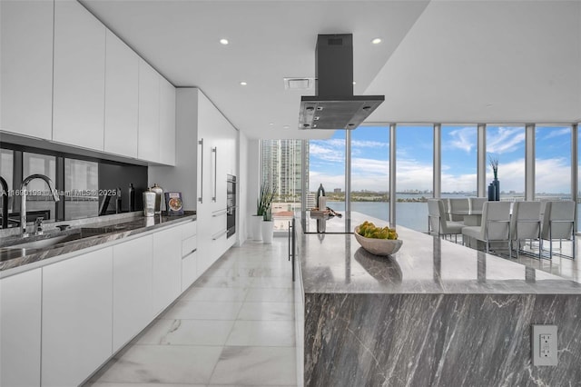 kitchen featuring floor to ceiling windows, sink, a water view, dark stone countertops, and white cabinets