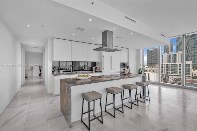 kitchen featuring a large island, a wealth of natural light, expansive windows, white cabinets, and island exhaust hood