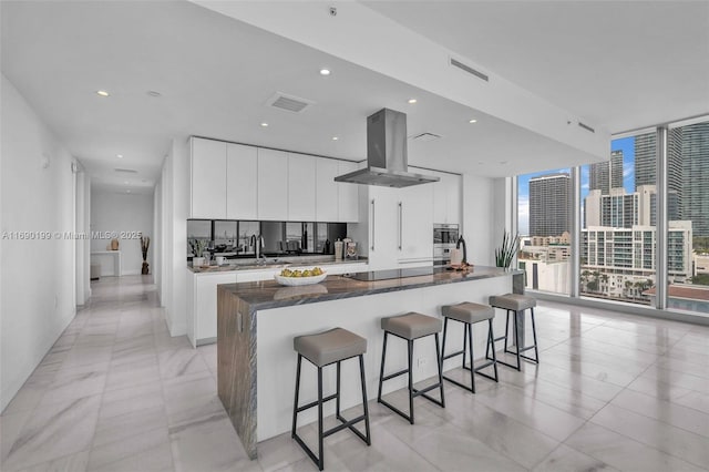 kitchen featuring a wall of windows, a kitchen breakfast bar, island exhaust hood, visible vents, and a spacious island