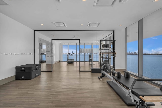 exercise room with expansive windows, a water view, wood finished floors, and visible vents