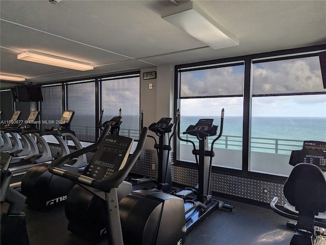 gym with a textured ceiling, a water view, and floor to ceiling windows