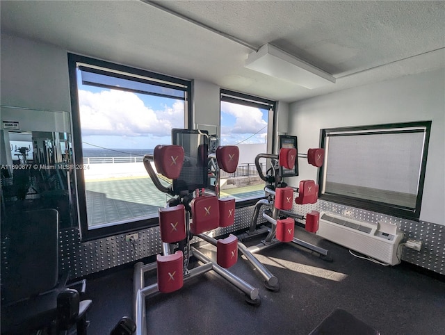 gym featuring a wall mounted AC, a water view, and a textured ceiling