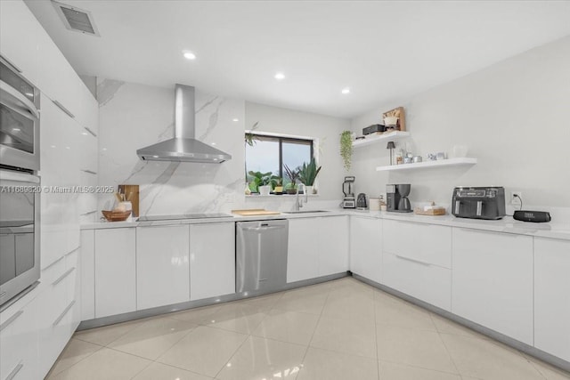 kitchen with visible vents, a sink, stainless steel appliances, wall chimney exhaust hood, and white cabinets