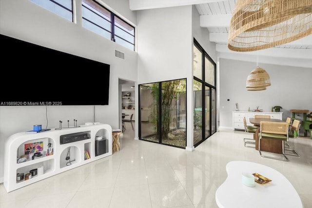 living room with beam ceiling, a high ceiling, visible vents, and tile patterned floors