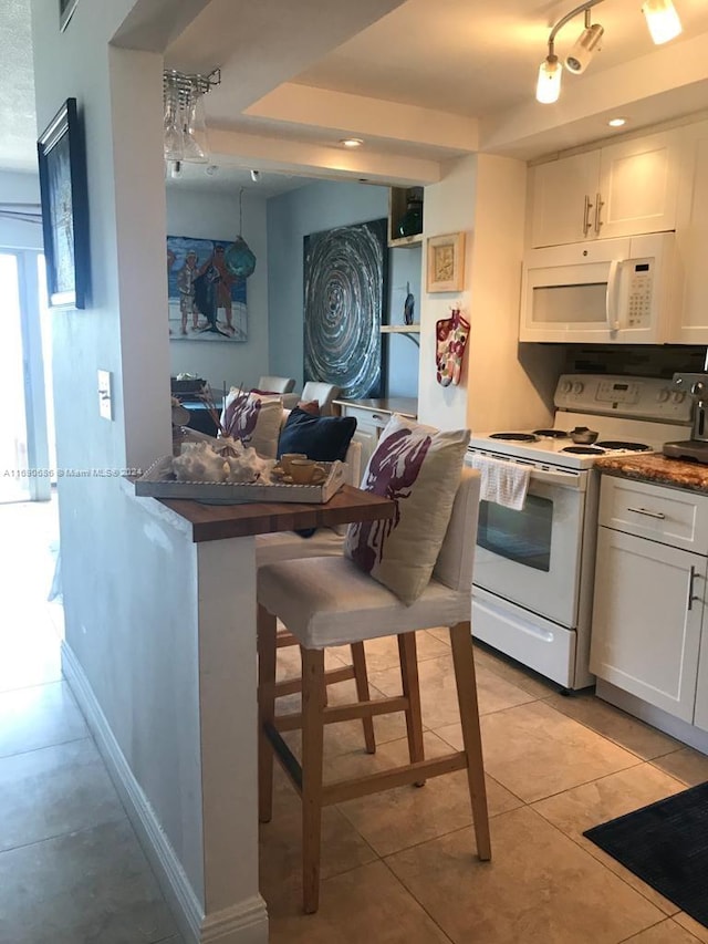 kitchen with white cabinets, a kitchen bar, light tile patterned floors, and white appliances